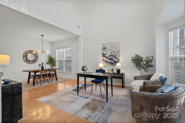 office space with hardwood / wood-style flooring, a towering ceiling, a chandelier, and decorative columns