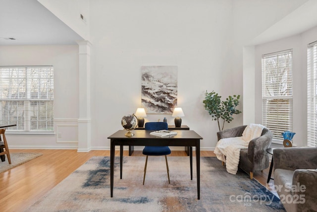 office with a healthy amount of sunlight, hardwood / wood-style floors, a high ceiling, and ornate columns