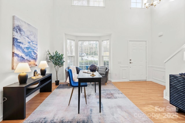 office area featuring a notable chandelier, a towering ceiling, and wood-type flooring