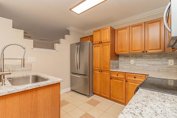 kitchen with stainless steel refrigerator, sink, decorative backsplash, ornamental molding, and light stone countertops