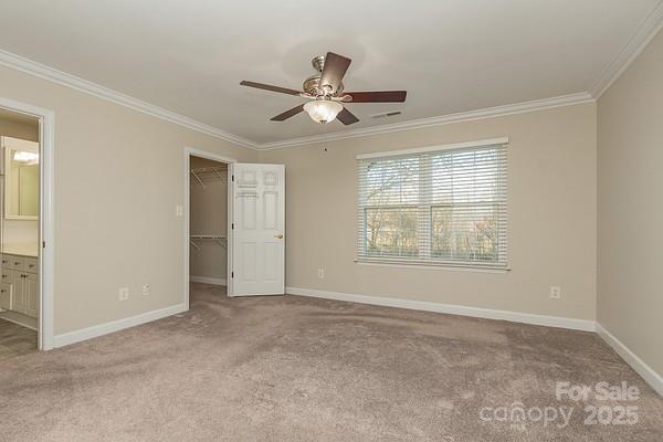 unfurnished bedroom with ensuite bath, a spacious closet, light carpet, ornamental molding, and a closet