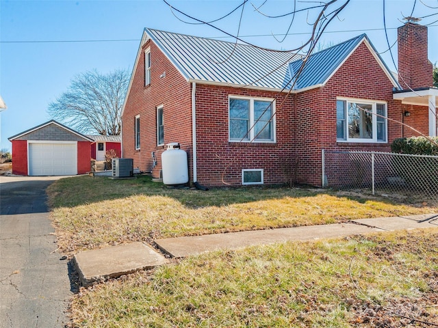 view of side of home featuring a standing seam roof, a yard, an outdoor structure, brick siding, and central AC unit