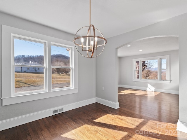 unfurnished dining area featuring a healthy amount of sunlight, wood-type flooring, and a notable chandelier