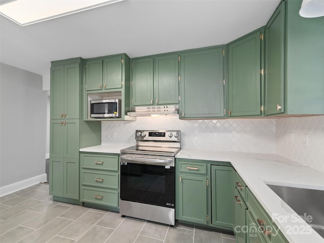 kitchen with appliances with stainless steel finishes, light stone countertops, green cabinets, and backsplash