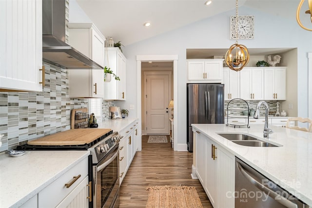 kitchen featuring appliances with stainless steel finishes, white cabinetry, sink, light stone countertops, and wall chimney range hood