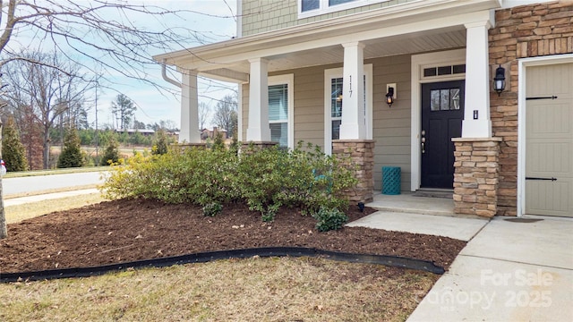 doorway to property with a garage, stone siding, and covered porch