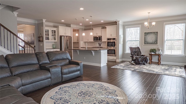 living area with dark wood-style floors, a notable chandelier, ornamental molding, and stairs