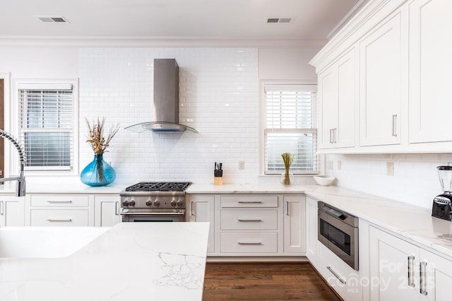 kitchen featuring wall chimney exhaust hood, crown molding, stainless steel appliances, light stone countertops, and white cabinets