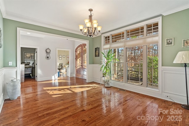 unfurnished dining area with hardwood / wood-style flooring, ornamental molding, and an inviting chandelier