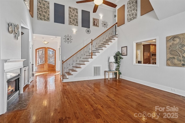 entrance foyer with ceiling fan, hardwood / wood-style floors, a high end fireplace, and french doors