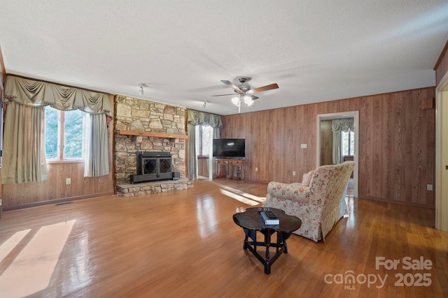 living room with a stone fireplace, hardwood / wood-style floors, a textured ceiling, and wood walls