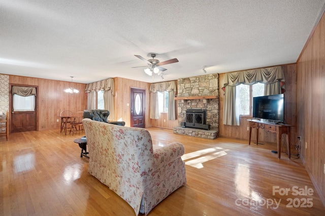 living room featuring a stone fireplace, ceiling fan with notable chandelier, light hardwood / wood-style flooring, and a textured ceiling