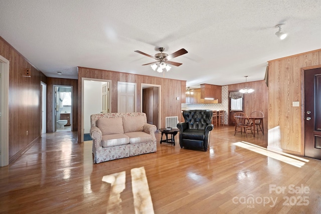 living room featuring wood-type flooring, wooden walls, ceiling fan with notable chandelier, and a textured ceiling