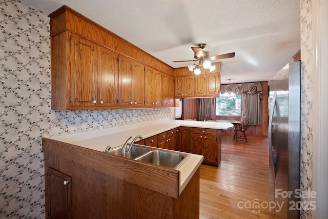 kitchen featuring stainless steel refrigerator, sink, hanging light fixtures, kitchen peninsula, and a textured ceiling