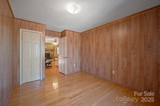 unfurnished bedroom with crown molding, hardwood / wood-style flooring, wooden walls, a textured ceiling, and a stone fireplace