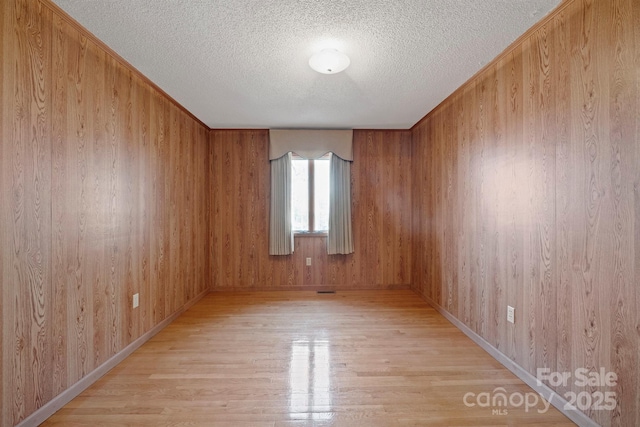 spare room with a textured ceiling, light hardwood / wood-style floors, and wood walls