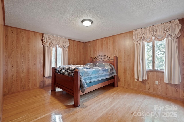 bedroom featuring multiple windows, light hardwood / wood-style floors, and wood walls