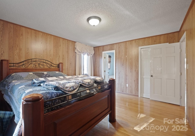 bedroom with a textured ceiling, wooden walls, and light hardwood / wood-style floors