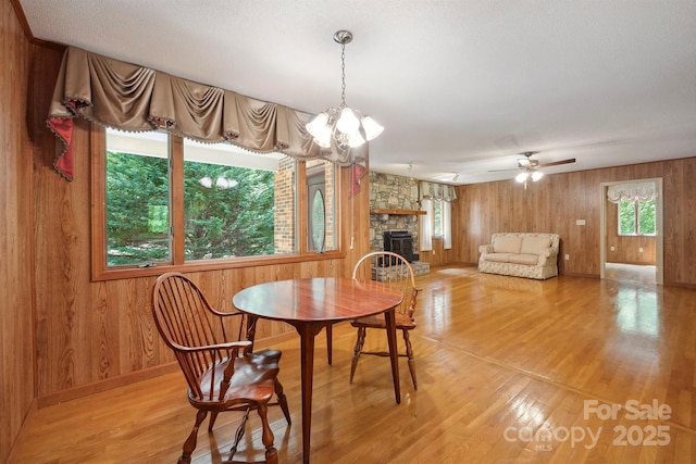 2076 Jay Clark Rd, Morganton, NC 28655 - dining area featuring ceiling fan with notable chandelier, light wood-type flooring, wood walls, baseboards, and a stone fireplace