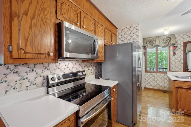 2076 Jay Clark Rd, Morganton, NC 28655 - kitchen featuring light wood finished floors, wallpapered walls, appliances with stainless steel finishes, and brown cabinetry