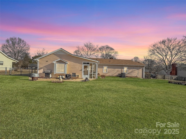 back house at dusk with a patio area and a lawn