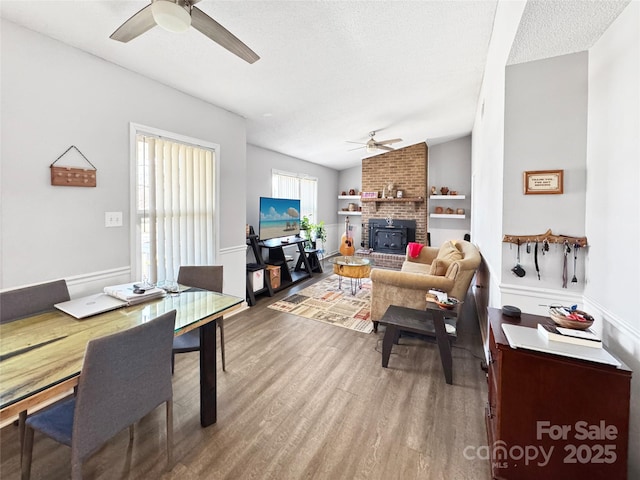 living room featuring vaulted ceiling, a textured ceiling, hardwood / wood-style flooring, ceiling fan, and a fireplace