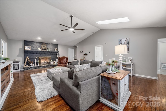 living room with lofted ceiling with skylight, a brick fireplace, dark hardwood / wood-style floors, and ceiling fan