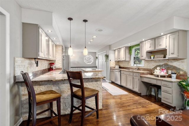 kitchen with appliances with stainless steel finishes, hanging light fixtures, tasteful backsplash, wood-type flooring, and light stone countertops