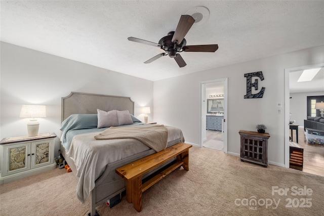 bedroom with ceiling fan, connected bathroom, light carpet, and a textured ceiling