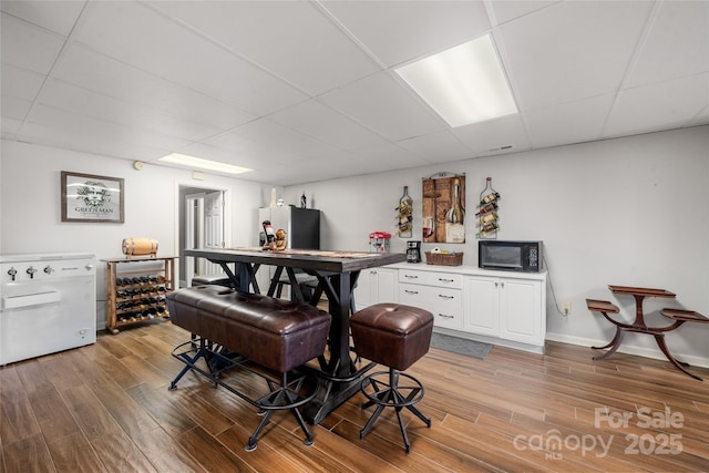 bar featuring wood-type flooring, a paneled ceiling, white cabinets, and refrigerator