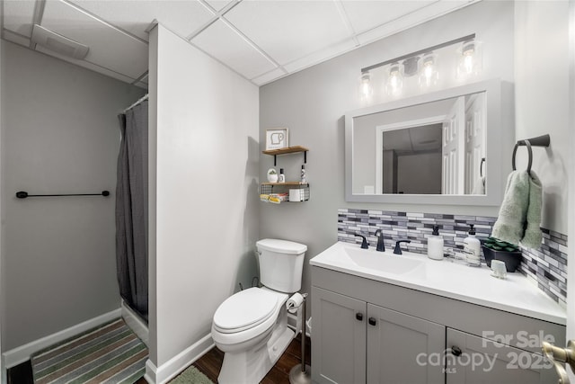 bathroom featuring a paneled ceiling, backsplash, vanity, walk in shower, and toilet