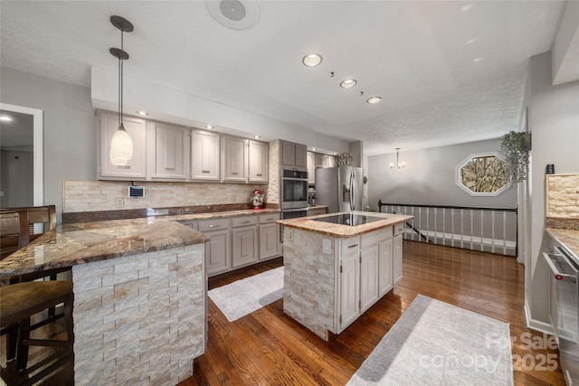 kitchen with hanging light fixtures, a center island with sink, dark hardwood / wood-style floors, stainless steel appliances, and light stone countertops