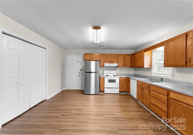 kitchen with sink, a textured ceiling, white appliances, and light hardwood / wood-style flooring