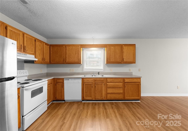 kitchen featuring white appliances, sink, a textured ceiling, and light wood-type flooring