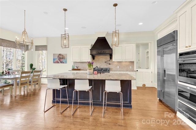 kitchen featuring backsplash, custom range hood, appliances with stainless steel finishes, an inviting chandelier, and white cabinetry