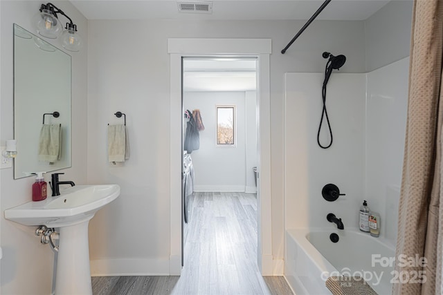 bathroom featuring hardwood / wood-style flooring, washing machine and clothes dryer, sink, and shower / bathtub combination with curtain