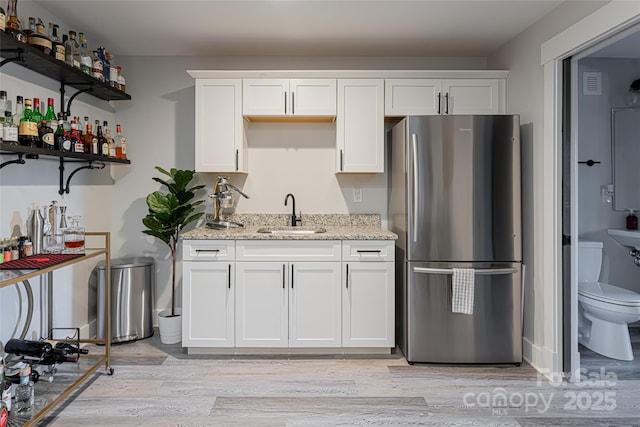 kitchen with sink, stainless steel refrigerator, light stone countertops, white cabinets, and light wood-type flooring