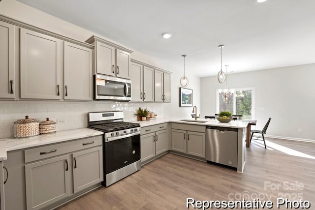 kitchen with sink, gray cabinets, appliances with stainless steel finishes, hanging light fixtures, and light stone counters