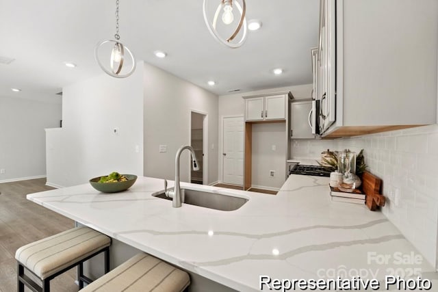 kitchen featuring pendant lighting, sink, light stone countertops, light hardwood / wood-style floors, and decorative backsplash