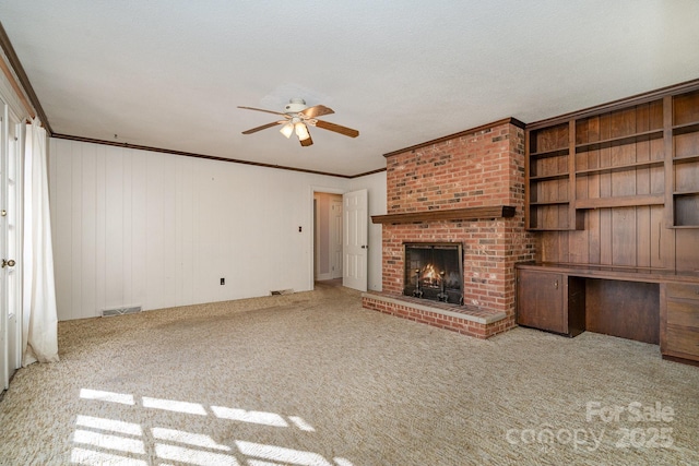 unfurnished living room featuring crown molding, built in desk, ceiling fan, a fireplace, and carpet