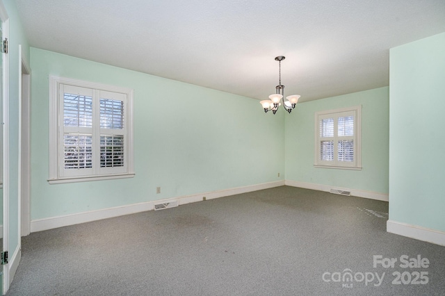 carpeted spare room featuring an inviting chandelier