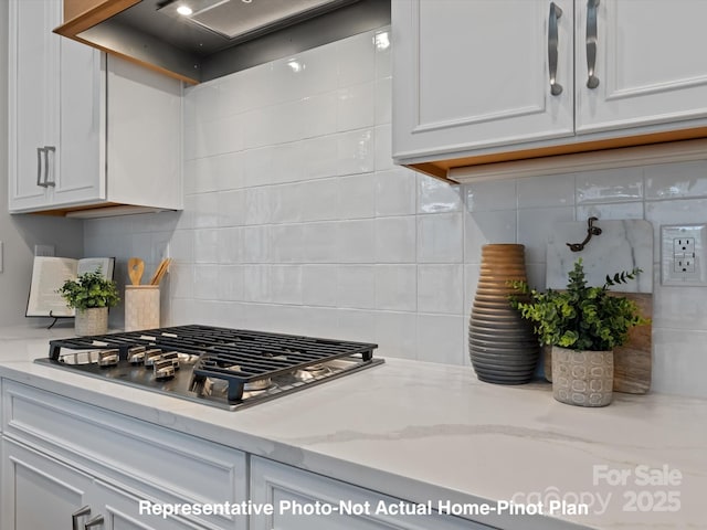 kitchen with light stone countertops, stainless steel gas cooktop, wall chimney range hood, and white cabinets