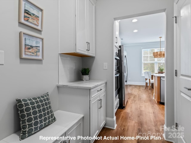 kitchen with appliances with stainless steel finishes, white cabinetry, light hardwood / wood-style floors, decorative backsplash, and decorative light fixtures