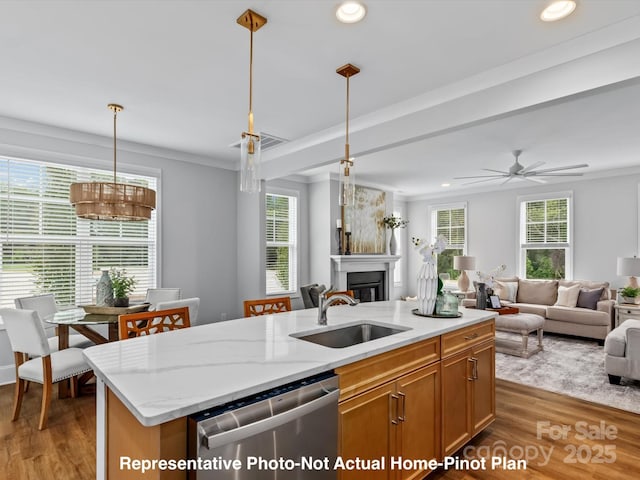 kitchen with pendant lighting, dishwasher, sink, light stone counters, and a center island with sink