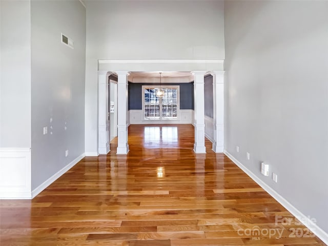 hall featuring a towering ceiling, hardwood / wood-style flooring, and ornate columns