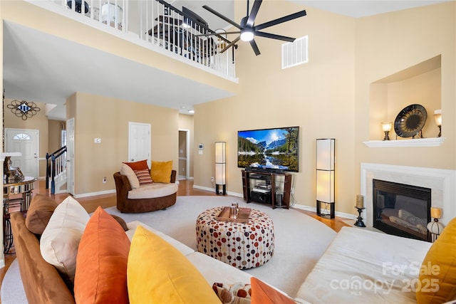 living room with ceiling fan, a high ceiling, and light wood-type flooring