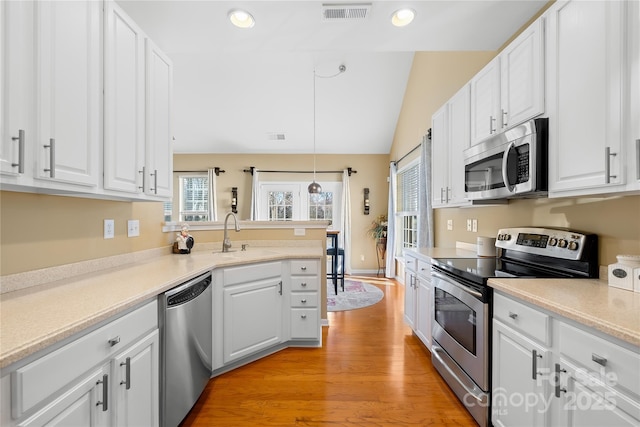 kitchen with stainless steel appliances, sink, white cabinetry, decorative light fixtures, and a healthy amount of sunlight