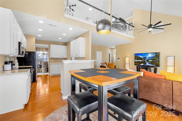 kitchen with a towering ceiling, white cabinetry, electric range, ceiling fan, and light hardwood / wood-style flooring