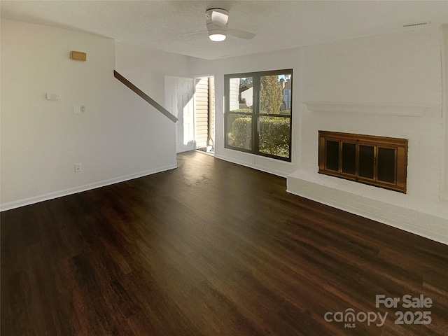 unfurnished living room featuring ceiling fan, dark hardwood / wood-style floors, a brick fireplace, and a textured ceiling