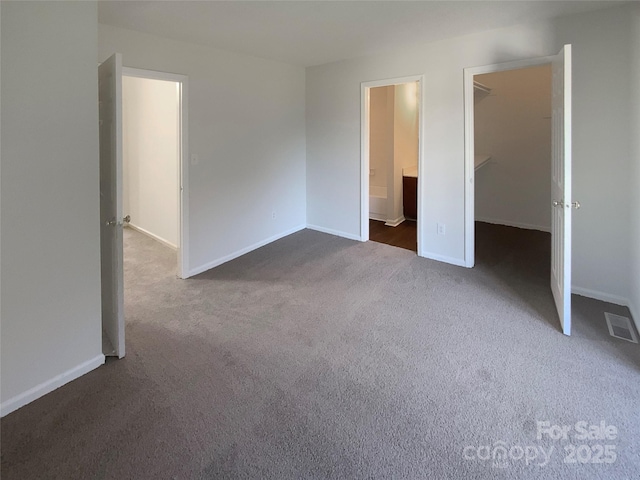 unfurnished bedroom with ensuite bathroom, a spacious closet, dark carpet, and a closet